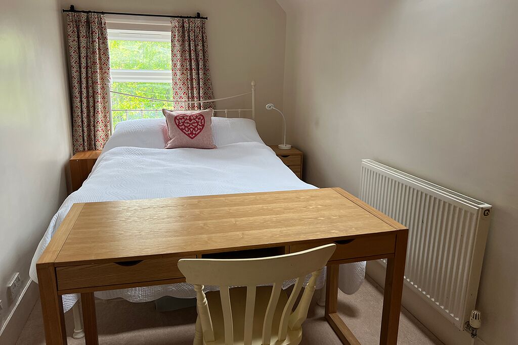 Bedroom with a bed, wooden table, chair and curtained window