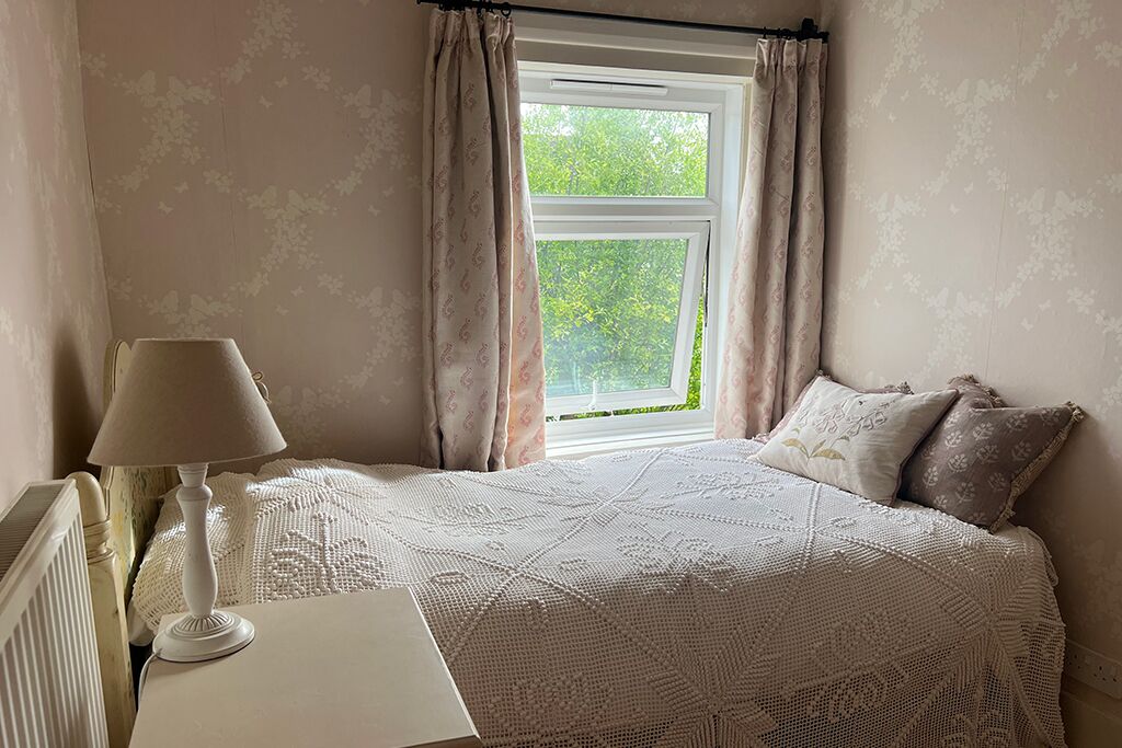 Bedroom with a bed, bedside table, lamp and curtained window